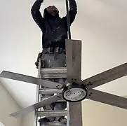Man on ladder installing modern ceiling fan, home improvement project.