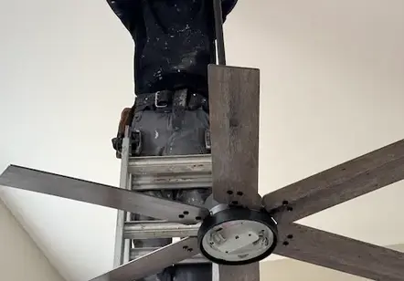 "Wesley's Workers technician installing a modern ceiling fan and light fixture in a residential home in Between, GA."