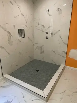 Modern walk-in shower with white marble tile and black floor.