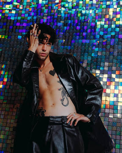 Stephen Sanchez posing shirtless under an open leather jacket against a sequin backdrop