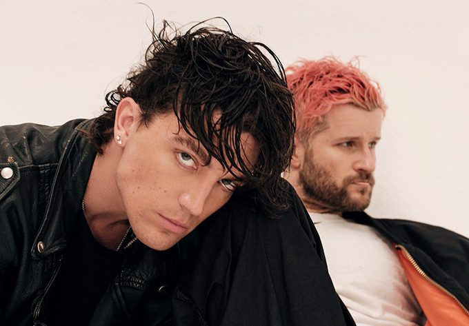 Paul Klein of LANY posing in a black leather jacket alongside bandmate Jake Goss