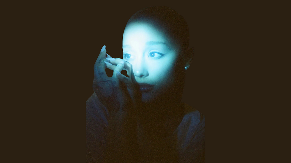 Ariana Grande in dim blue lighting with her hand near her face, promotional photo from her Eternal Sunshine era