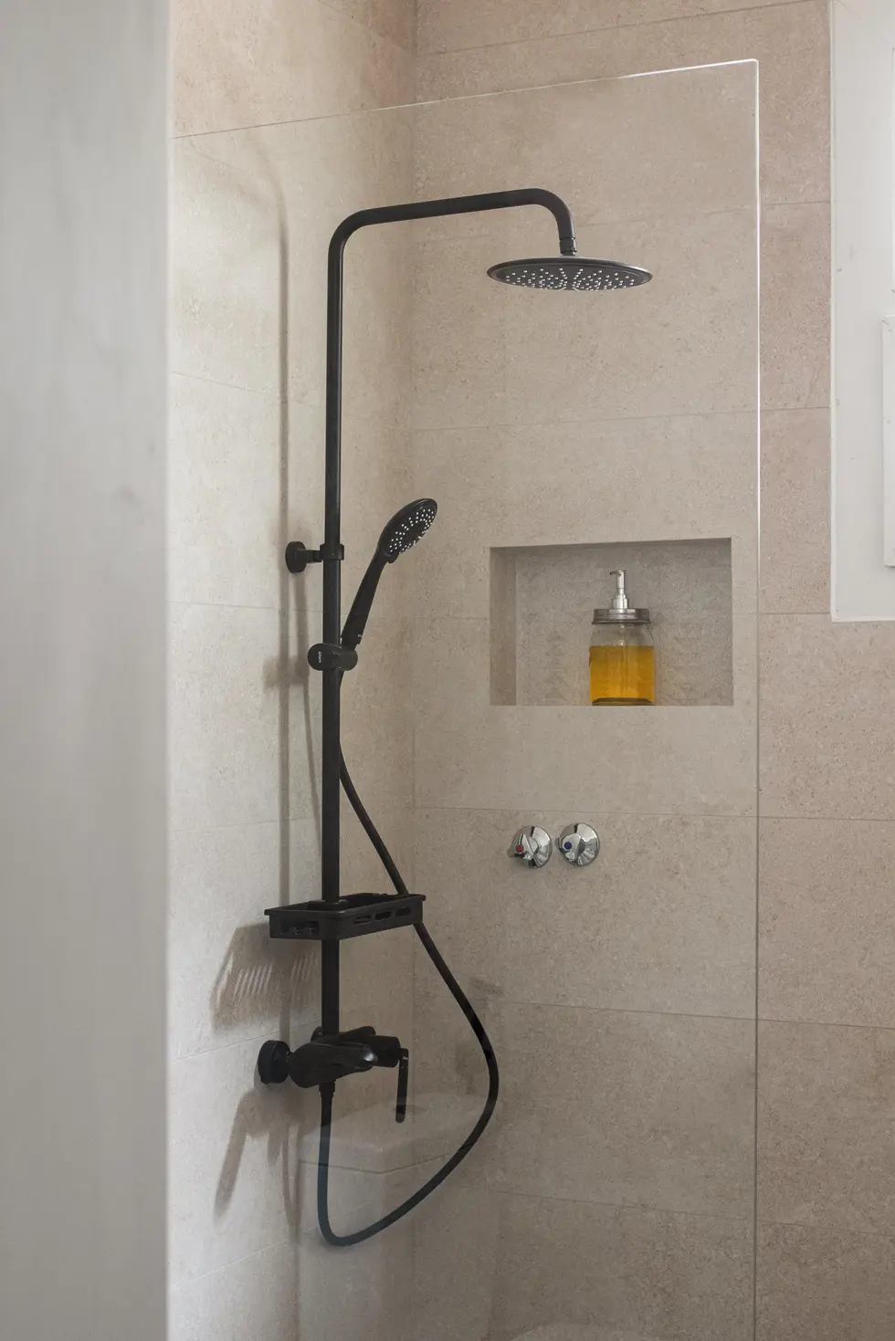 Modern shower with black fixtures, beige tiles, and built-in niche, designed by Miriam Roberts for Roberts Renovation.