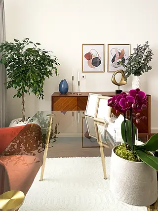 "Sophisticated dining area with a glass table featuring gold accents, vibrant orchids, and a warm wood sideboard adorned with abstract art and greenery. This interior, originally designed in Doha, showcases a blend of modern elegance and warmth, demonstrating how Roberts Renovations can bring similar refined and inviting designs to homes in Wakefield."