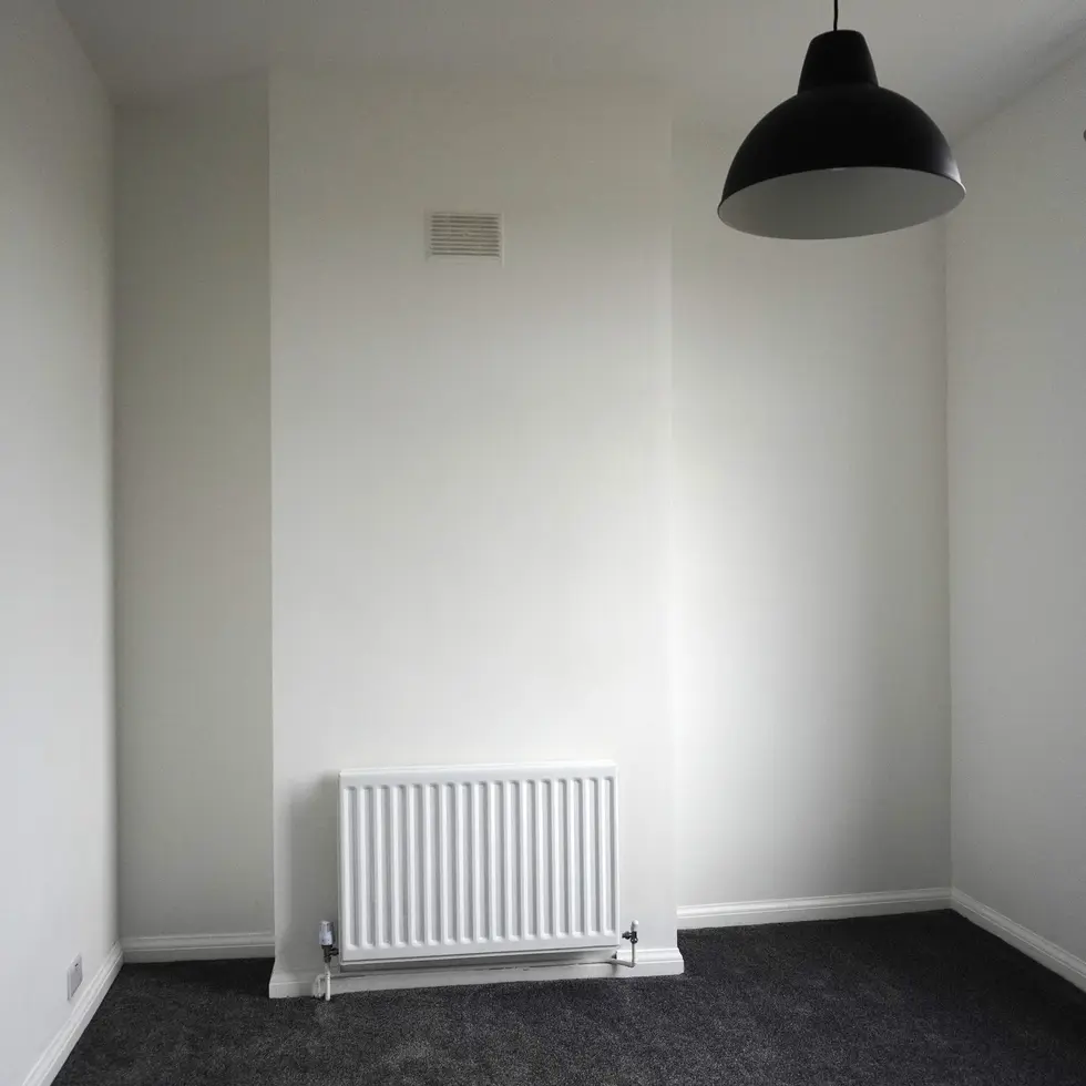 Minimalist refurbished bedroom with grey carpet, white walls, and large window in a mid-terrace house in Leeds, designed by Miriam Roberts.