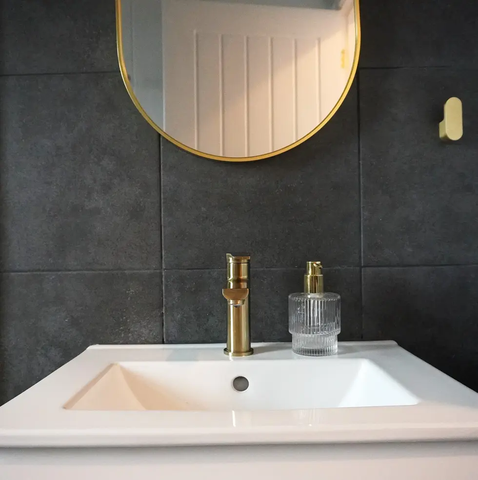Modern wet room with dark tiles, brass fixtures, and a white vanity unit in a mid-terrace house in Leeds, designed by Miriam Roberts.