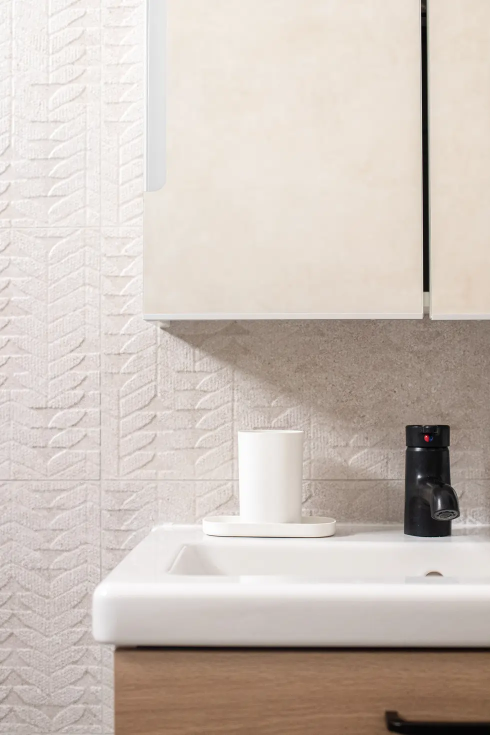 Minimalist bathroom with light beige tiles, wood vanity, black fixtures, and a mirrored cabinet, designed by Miriam Roberts for Roberts Renovation.