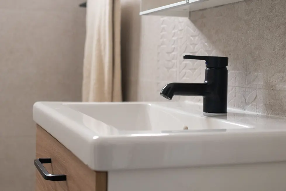 Modern bathroom with wood vanity, black tap, textured beige tiles, and mirrored cabinet, designed by Miriam Roberts for Roberts Renovation.