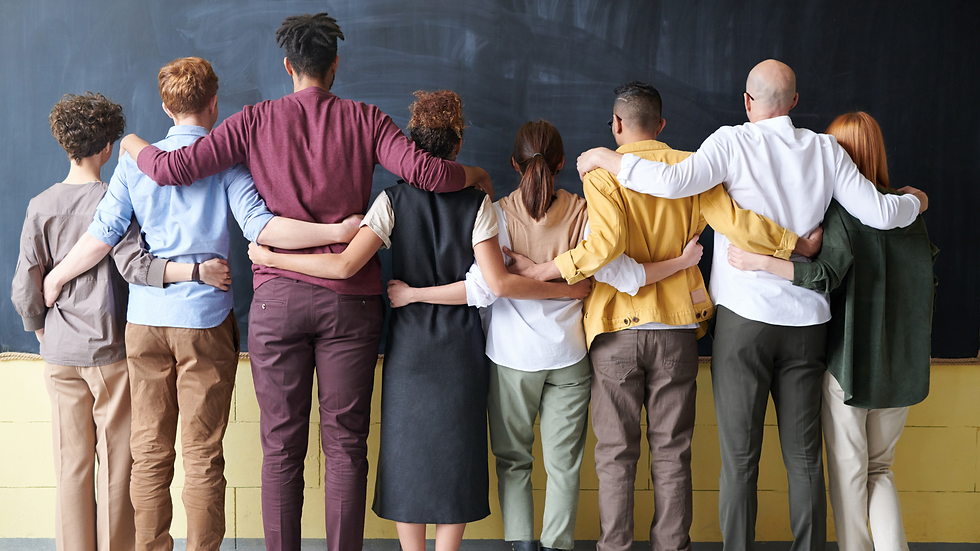 Eight people standing in a line with arms around each other, facing a blackboard. Diverse clothing and hairstyles, showing unity.