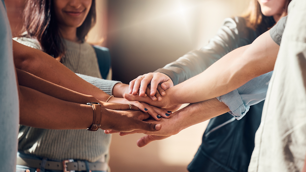 Diverse hands stack in unity, expressing teamwork and camaraderie. Soft light and casual wear create a warm, collaborative atmosphere.