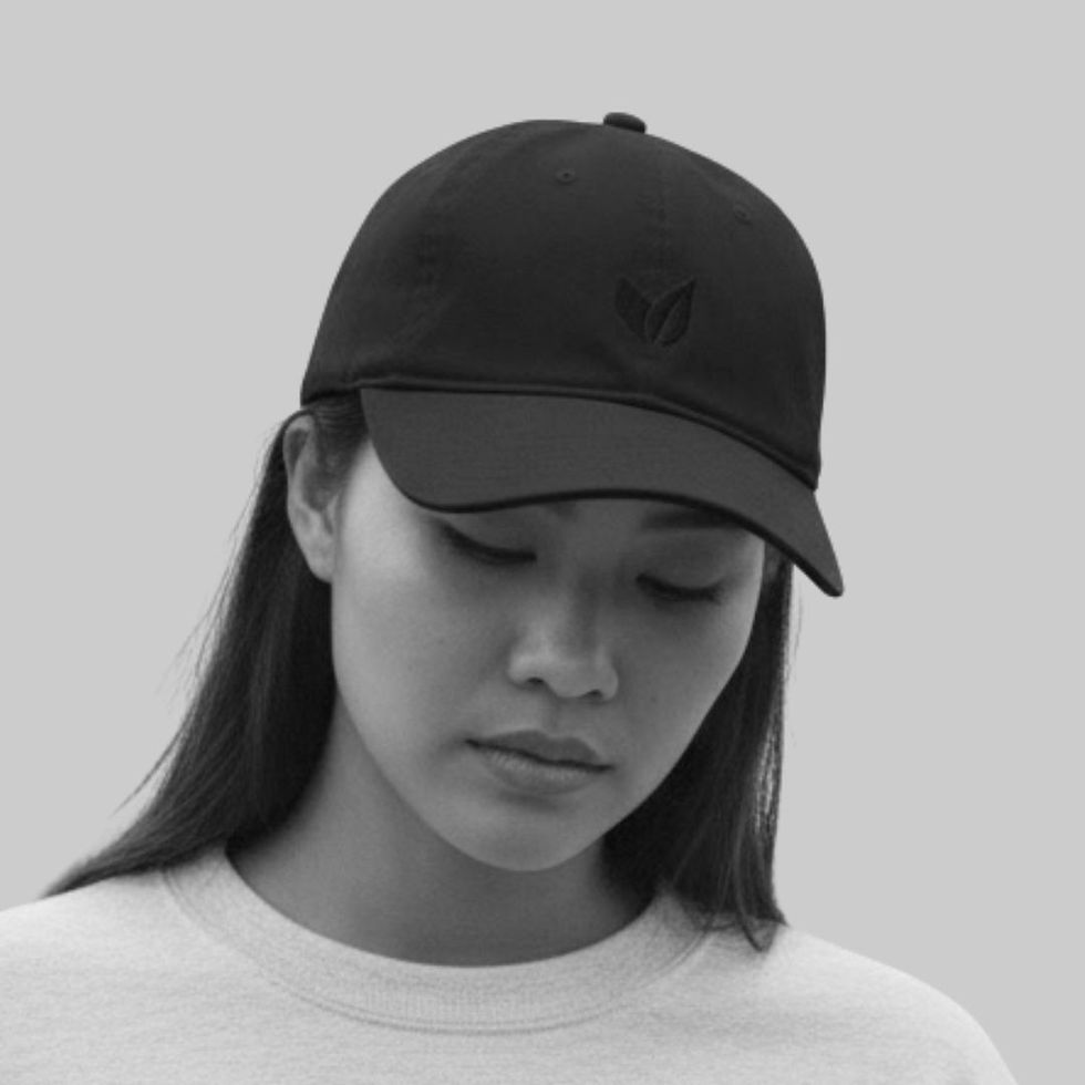 Model wearing black unisex baseball cap with tonal leaf embroidery, shown in a minimalist studio setting