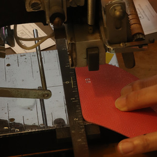 close-up shot of the name stamping process on the leather. A hand is holding the leather in place while the machine is stamping, The stamped letters are golden in color..