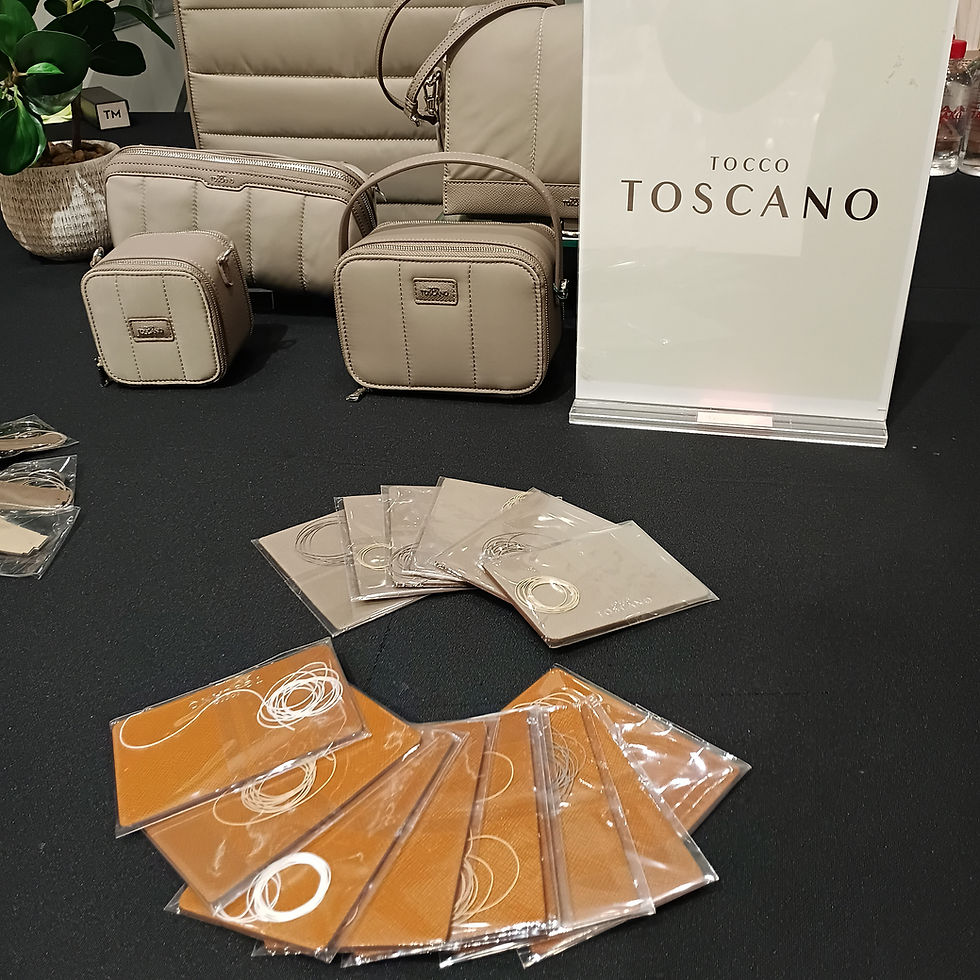 Beige bags and small pouches on black surface, with "Tocco Toscano" sign. Circular display of orange and beige cardholders in plastic covering.