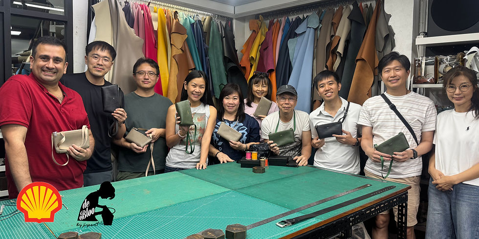 Smiling group holding purses in a room with colorful hanging leathers. A green worktable and Shell logo visible. Joyful and creative atmosphere.