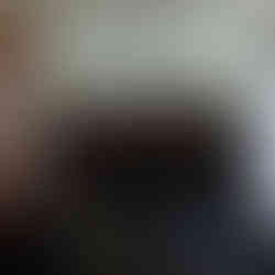 4 smiling women stands in front of a wall with the word Prada on it. 2 people are wearing aprons, and the other 2 are wearing suits. They are making heart signs with their hands.