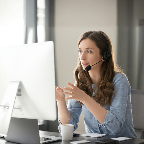 Auf dem Bild ist eine Frau mit Headset vor einem PC zu sehen.