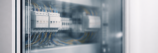Nahaufnahme eines modernen elektrischen Schaltschranks mit ordentlich verkabelten Leitungsschutzschaltern und Sicherungen hinter einer transparenten Glasfront.