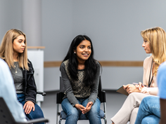 A photo of a teenage girl talking in a circle of other young people