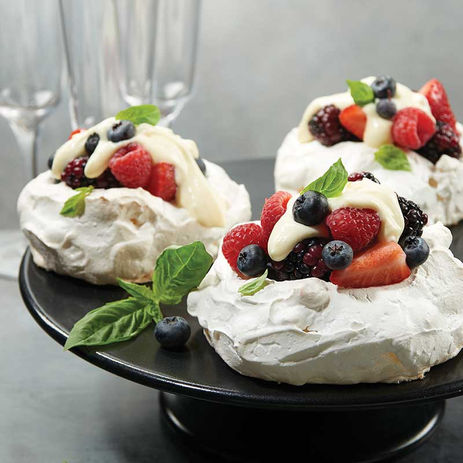Mini pavlovas topped with assorted berries and cream on a black cake stand