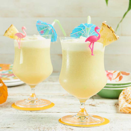 Two tropical piña coladas garnished with mini umbrellas and pineapple slices