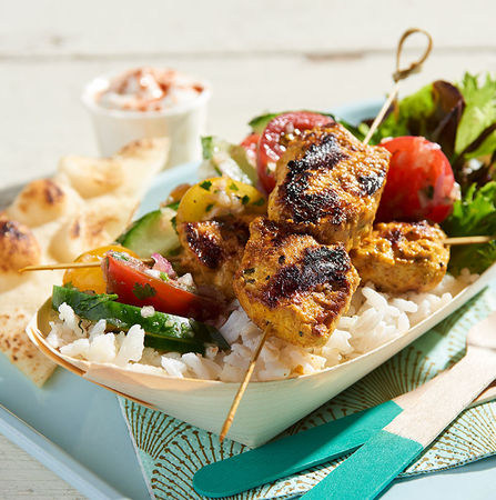 Grilled chicken skewers served over rice with mixed vegetables and flatbread on the side