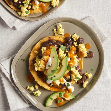 ortilla topped with scrambled eggs, salsa, cheese, meat, and fresh avocado slices