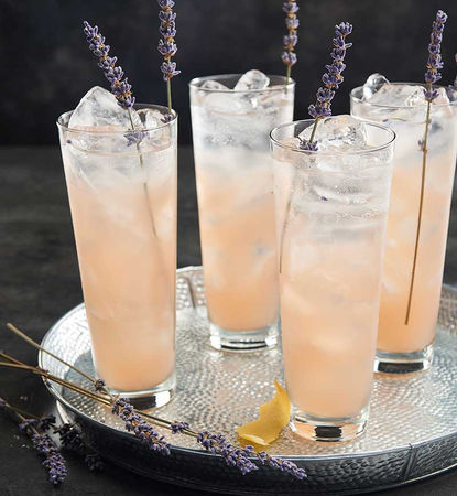 Tall lavender-infused cocktails with ice, served on a silver tray and garnished with lavender sprigs