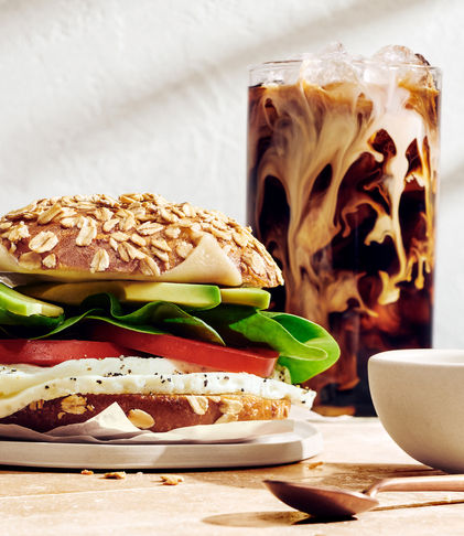 A healthy veggie burger with greens and cheese served alongside a glass of iced coffee