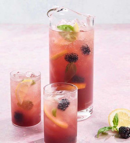 all glasses of citrus cocktails with floating blackberries and lemon slices on a pink background