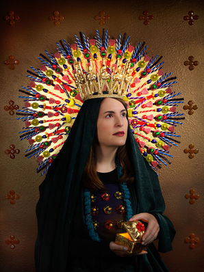 A woman dressed in dark, regal robes wears an ornate halo-like crown made of colorful lollipops and candy sticks, holding a gilded gift against a rich, textured background.