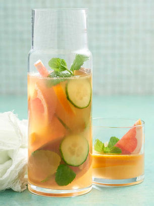 A glass pitcher of cucumber mint iced tea with a matching glass on a light background