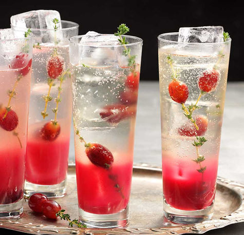 Sparkling cocktails with berries and thyme served in tall glasses on a silver tray