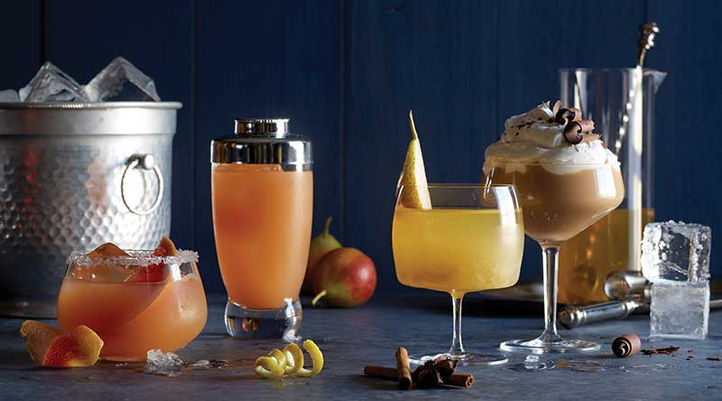 An assortment of autumn cocktails with garnishes, surrounded by cocktail tools and ice bucket