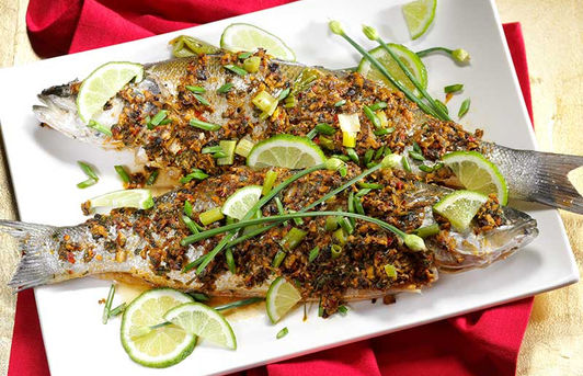 Two whole roasted fish garnished with lime slices and green herbs on a white platter