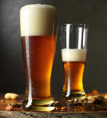 Two tall glasses of craft beer with thick foam on a dark wooden surface