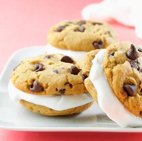 Soft chocolate chip cookies sandwiching a thick layer of fluffy marshmallow filling, served on a white plate against a pastel pink background.