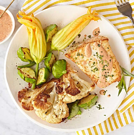 Grilled salmon served with cauliflower, Brussels sprouts, and squash blossoms on a striped plate