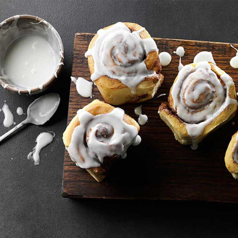 Small cinnamon rolls topped with icing on a dark wooden board
