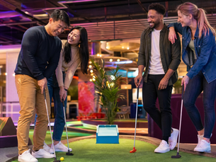 Two couples playing mini golf together at a modern indoor venue, laughing and having fun