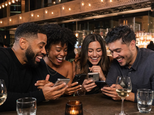 Two couples at a restaurant laughing together while looking at their phones in a group chat