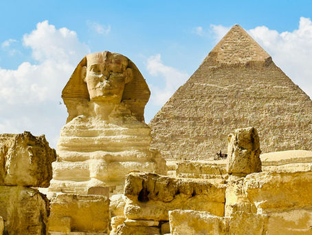 Sphinx and Pyramid bathed in sunlight against a bright blue sky with fluffy clouds in the background, conveying an ancient, timeless mood.