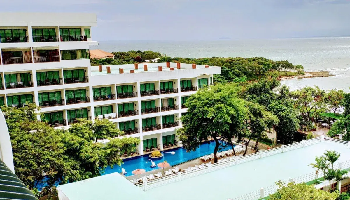 Панорамный вид на корпус Cosy Beach Hotel, окруженный тропической зеленью. Длинный бассейн с шезлонгами вдоль фасада и живописный вид на море
