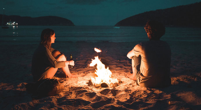 Zwei Personen am Lagerfeuer am Strand bei Nacht