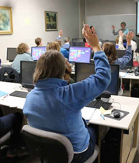 Woman raises hand in staff training group while seated at computer