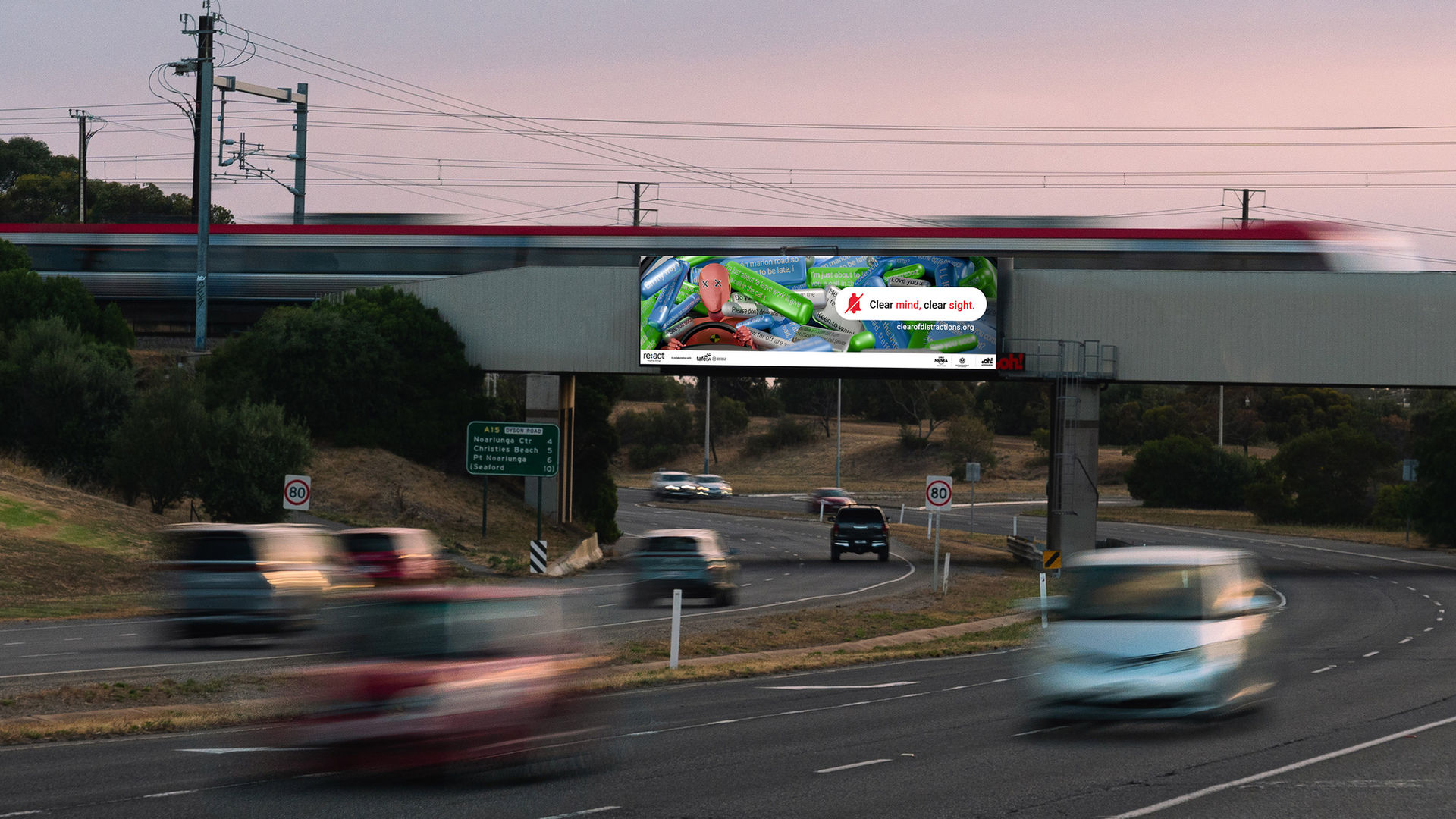 Picture of a billboard with cars travelling underneath, and a train on the overpass. The billboard shows a road safety campaign of a crash test dummy being surrounded by text messages, highlighting the dangers of distracted driving - by Benjamin Anstey
