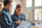 Project manager or homeowner reviewing budget and timeline with builder at a construction site, both looking at a clipboard