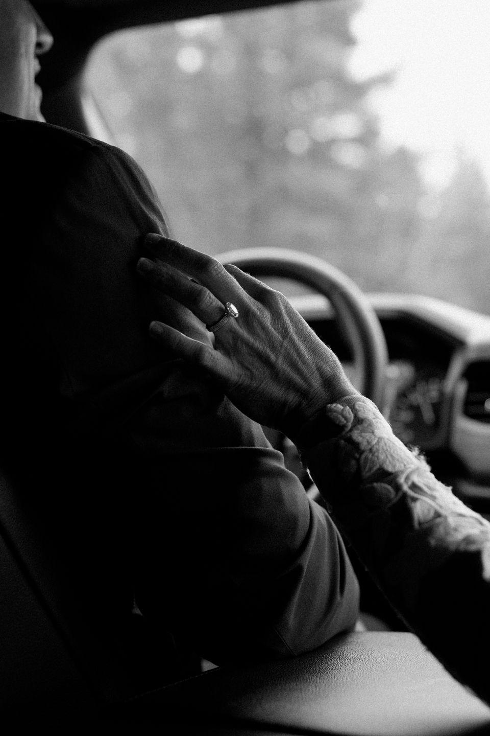 bride puts hand on grooms shoulder while riding in the car