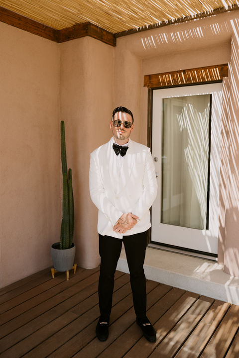 grooms stands in his white suit with cool shadows