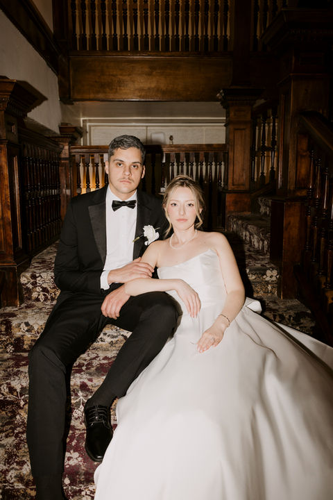 editorial moody photo of bride and groom sitting on wood staircase in wedding venue