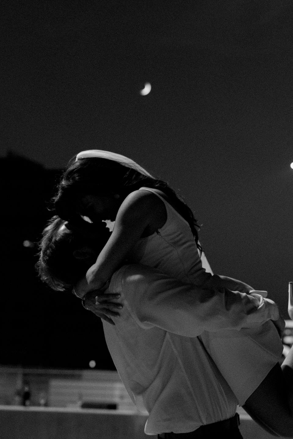 moody photo of bride and groom kissing with moon in the background